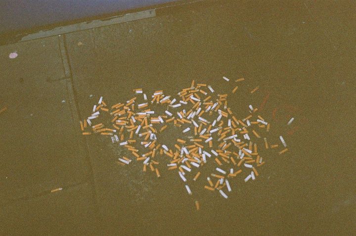 grainy film photo of a pile of cigarettes laying on the sidewalk